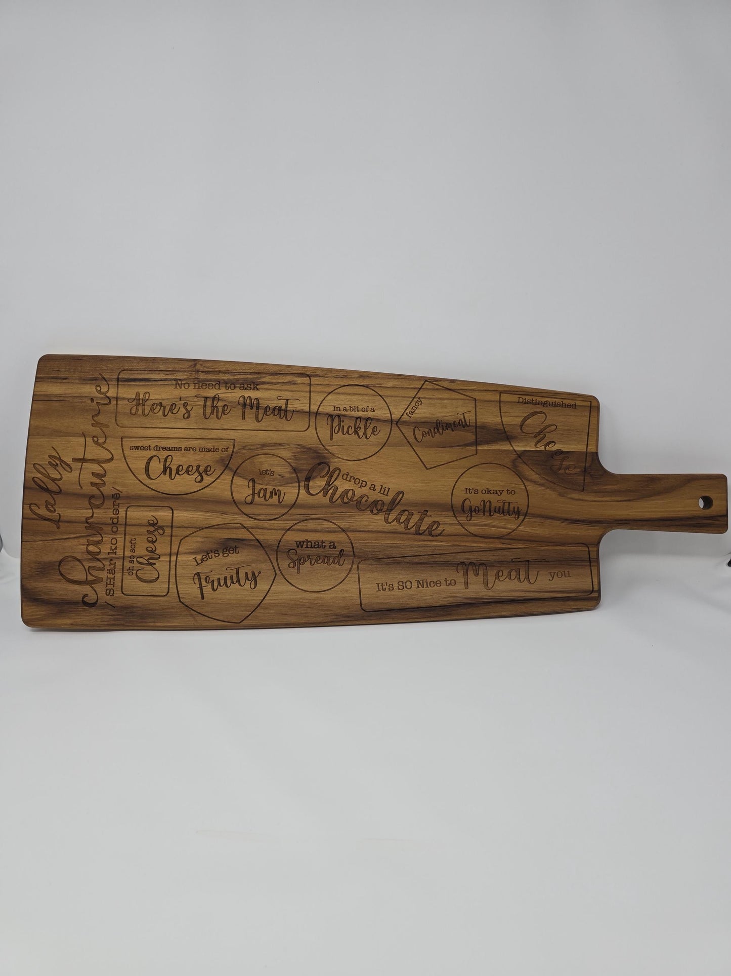 Personalized engraved wooden cutting board with a name and the word &quot;charcuterie&quot; engraved on it, featuring designated spots for meats, cheeses, crackers, and other charcuterie items